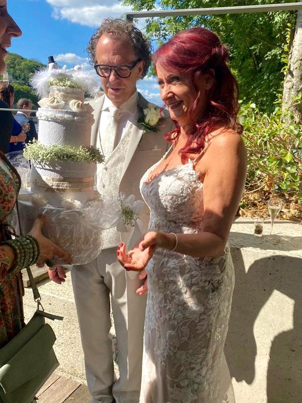 Real-life Pippi bride Bianca looks at the wedding cake with her husband. She wears a long lace wedding gown with delicate spathetti straps. The lining of the dress is mocha color and the lace over it is ivory white.